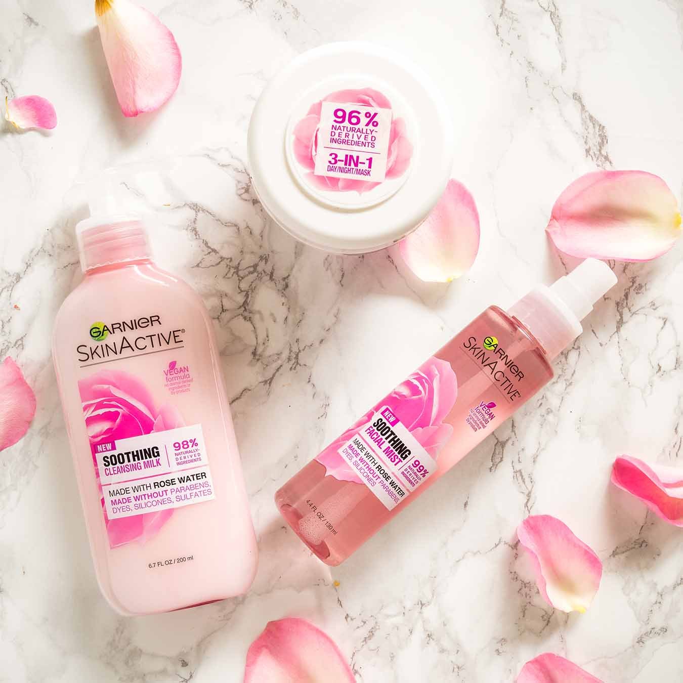 Garnier SkinActive Soothing Cleansing Milk, SkinActive Soothing Facial Mist, SkinActive 3-in-1 Day/Night Mask on white marble with pink rose petals.